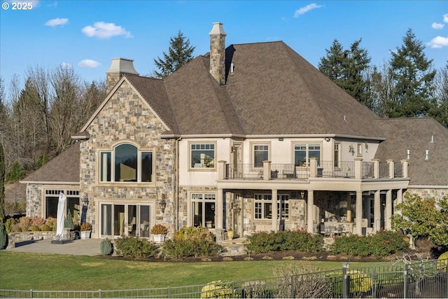 rear view of house with a balcony, a lawn, and a patio area