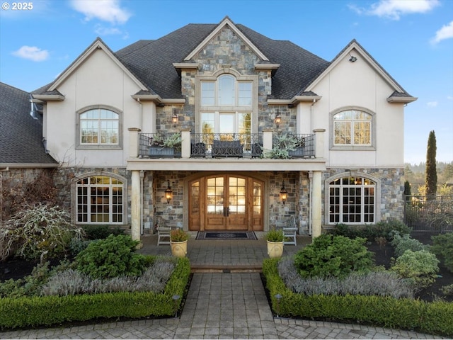 french country home with a porch, a balcony, and french doors