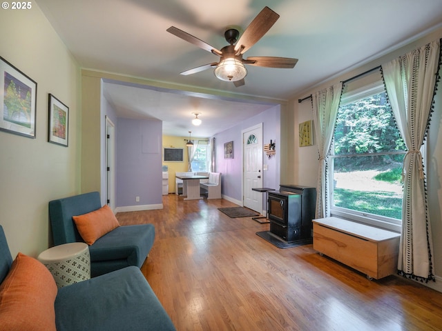 living room with a wood stove, a ceiling fan, light wood-style floors, and baseboards