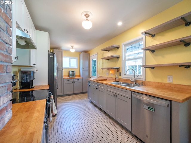 kitchen with wood counters, stainless steel appliances, a sink, and open shelves