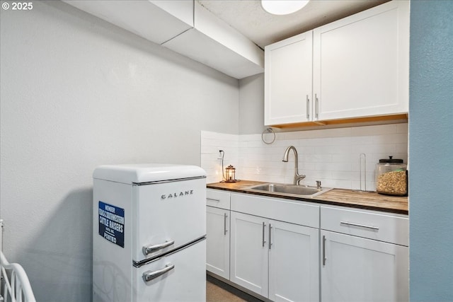 kitchen featuring wooden counters, white fridge, a sink, backsplash, and white cabinets