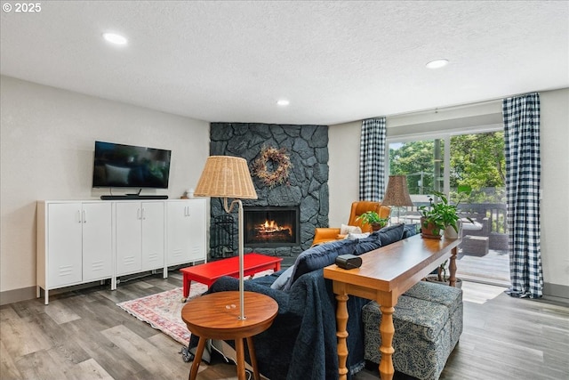 living room with a textured ceiling, wood finished floors, recessed lighting, a stone fireplace, and baseboards