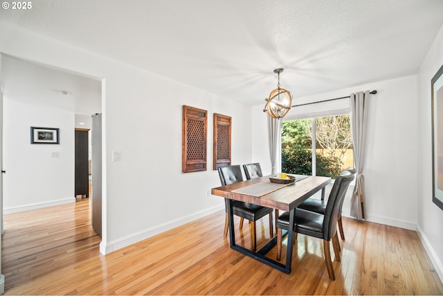 dining area with a textured ceiling, light wood-type flooring, an inviting chandelier, and baseboards