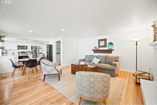 living room featuring light wood finished floors, baseboards, a fireplace with raised hearth, a textured ceiling, and recessed lighting