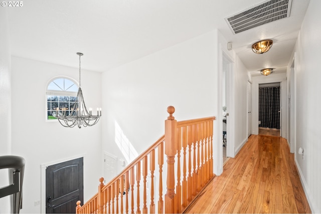 corridor featuring a notable chandelier, visible vents, an upstairs landing, light wood-type flooring, and baseboards