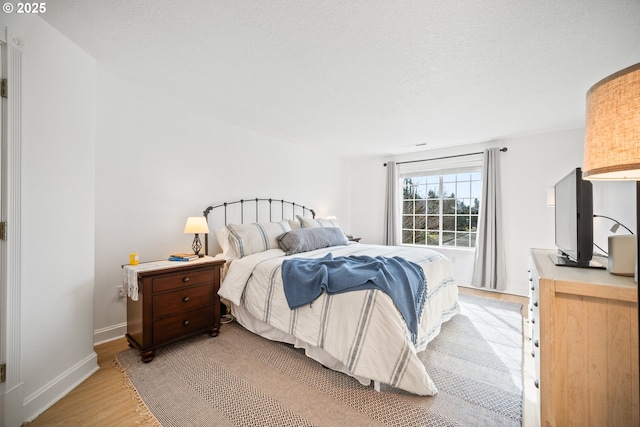 bedroom with light wood-type flooring, baseboards, and a textured ceiling