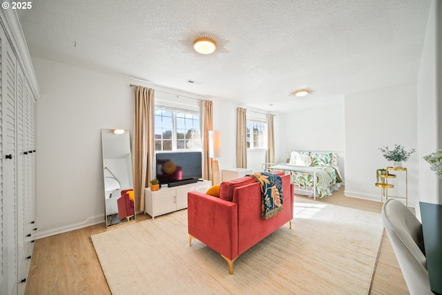 living area with baseboards, visible vents, a textured ceiling, and light wood finished floors