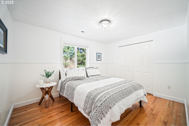 bedroom featuring wood-type flooring, a textured ceiling, baseboards, and a closet