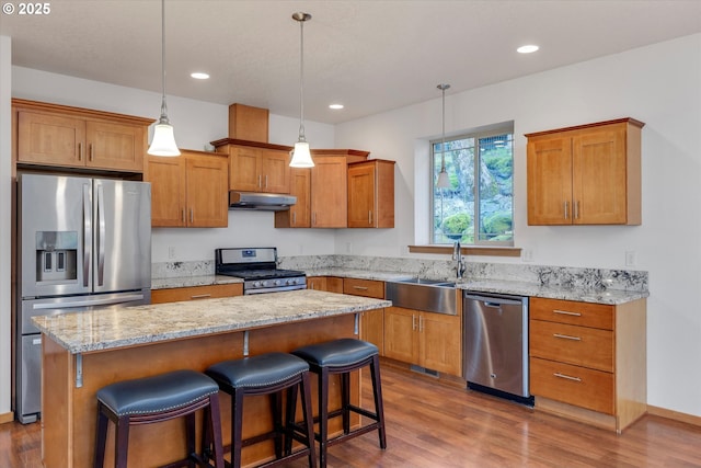 kitchen with wood-type flooring, stainless steel appliances, hanging light fixtures, a kitchen island, and sink