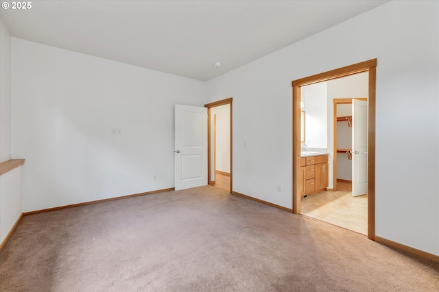 unfurnished bedroom featuring ensuite bathroom, light colored carpet, and a spacious closet