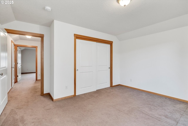 unfurnished bedroom with light colored carpet, vaulted ceiling, and a closet