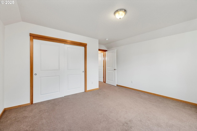 unfurnished bedroom featuring lofted ceiling, a closet, and light carpet