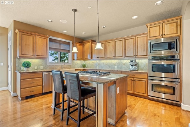 kitchen with pendant lighting, a kitchen island, a kitchen breakfast bar, stainless steel appliances, and light stone countertops