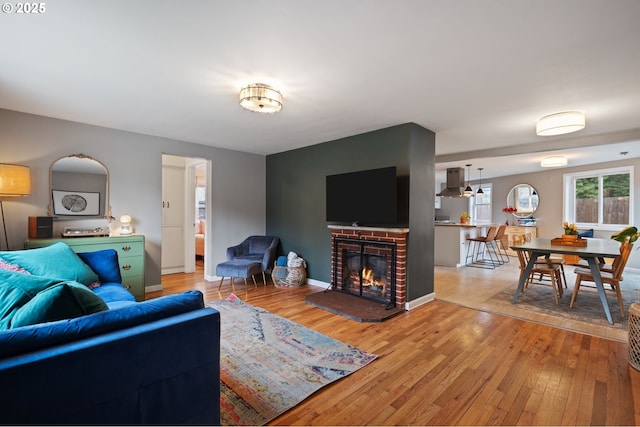 living area featuring a brick fireplace, light wood-style flooring, and baseboards