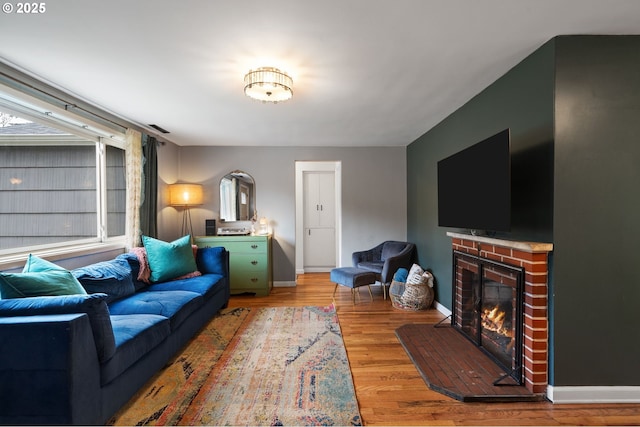 living room featuring light wood finished floors, a brick fireplace, visible vents, and baseboards