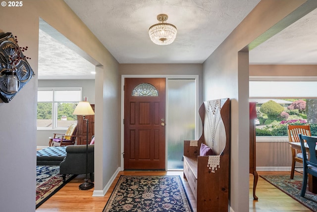 foyer featuring wood finished floors, a textured ceiling, a chandelier, and baseboards