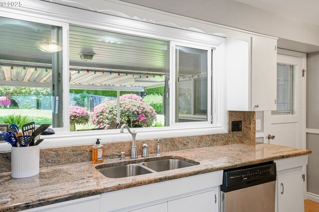 kitchen with stainless steel dishwasher, a sink, white cabinets, and light stone countertops