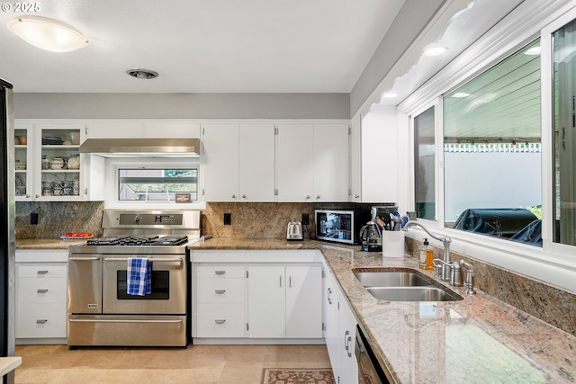kitchen featuring range with two ovens, a sink, under cabinet range hood, light stone countertops, and tasteful backsplash