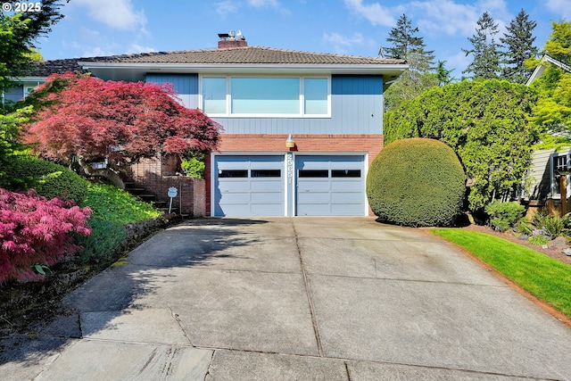 view of front of home featuring a garage, a tiled roof, concrete driveway, a chimney, and brick siding
