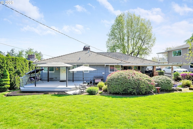 back of property with a chimney, a lawn, a deck, and a tiled roof