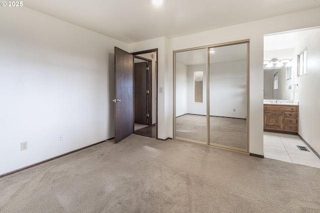 unfurnished bedroom with light colored carpet, ensuite bath, and a closet