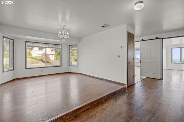 spare room featuring hardwood / wood-style flooring, a barn door, and a notable chandelier