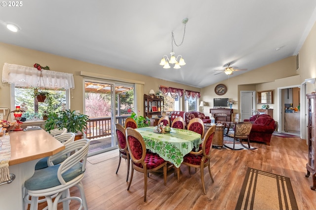 dining room featuring a fireplace, lofted ceiling, ceiling fan with notable chandelier, and light wood-style floors