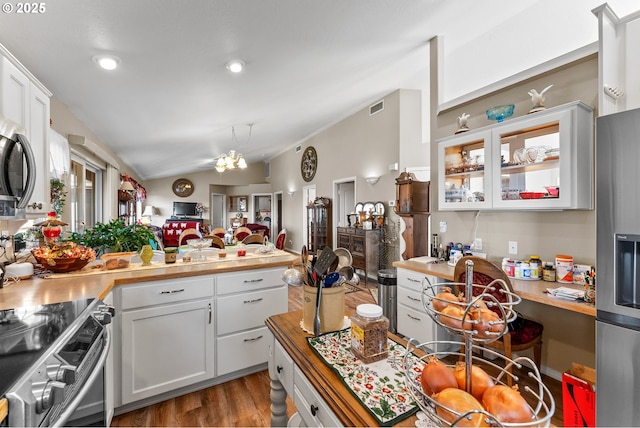 kitchen with visible vents, wood finished floors, appliances with stainless steel finishes, a peninsula, and lofted ceiling