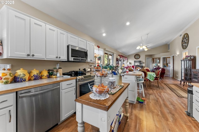 kitchen with light wood finished floors, a chandelier, open floor plan, vaulted ceiling, and appliances with stainless steel finishes