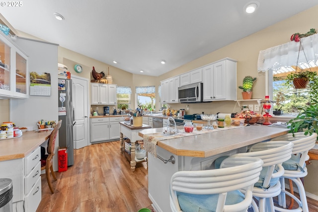 kitchen featuring light wood-style flooring, stainless steel appliances, a peninsula, white cabinets, and light countertops