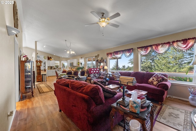 living area featuring lofted ceiling, ceiling fan with notable chandelier, and light wood-type flooring