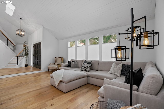 living room featuring light wood-style flooring, a notable chandelier, vaulted ceiling, and stairway