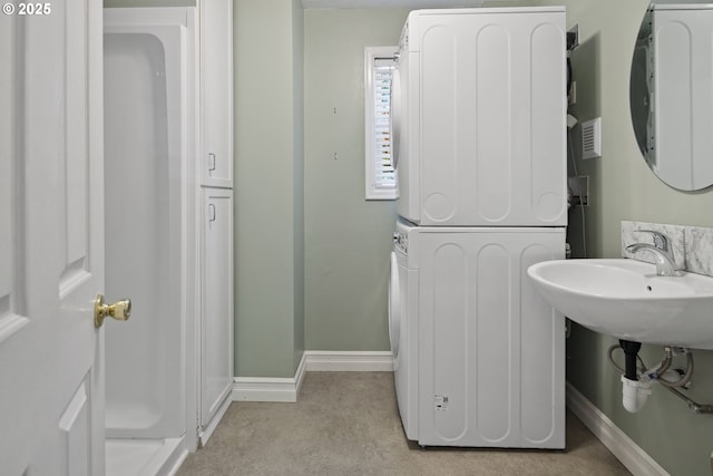 bathroom featuring estacked washer and dryer, baseboards, and a sink