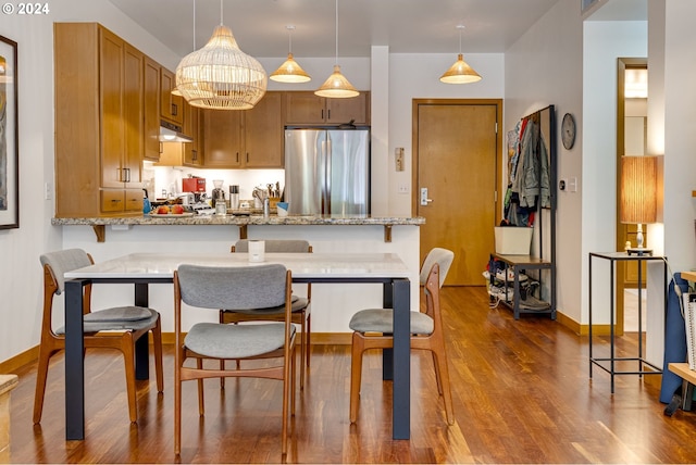 kitchen with freestanding refrigerator, pendant lighting, a peninsula, dark wood-style floors, and under cabinet range hood