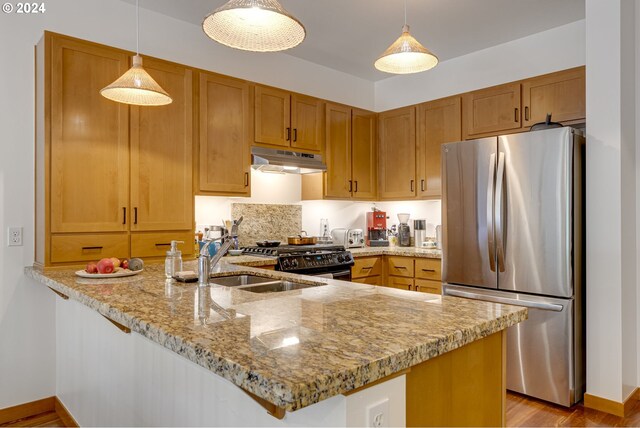kitchen with freestanding refrigerator, a peninsula, light stone countertops, under cabinet range hood, and range with gas cooktop