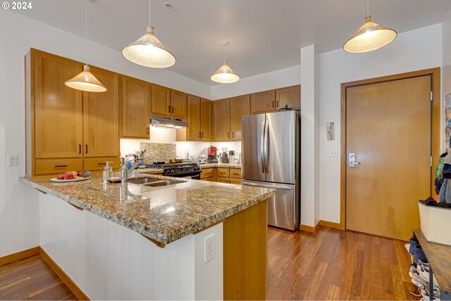 kitchen featuring freestanding refrigerator, a peninsula, wood finished floors, gas range, and under cabinet range hood