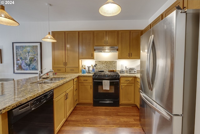 kitchen featuring wood finished floors, light stone countertops, under cabinet range hood, a sink, and black appliances