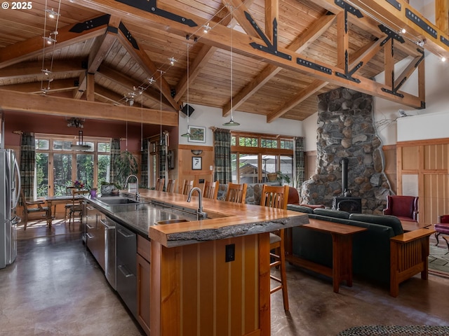 kitchen with wood ceiling, a wood stove, concrete flooring, a center island with sink, and a sink