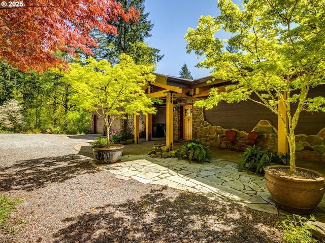 rear view of property featuring stone siding, a patio area, and gravel driveway
