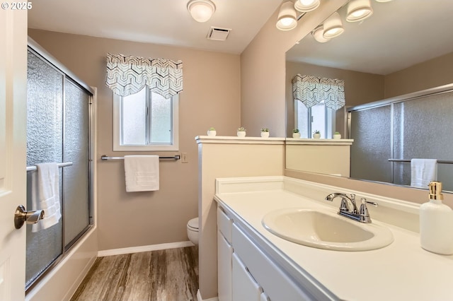 full bathroom featuring wood finished floors, vanity, toilet, baseboards, and bath / shower combo with glass door