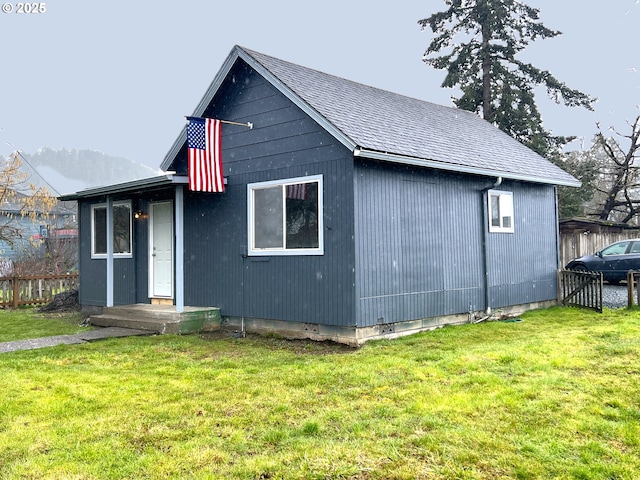 exterior space featuring a lawn, a shingled roof, and fence