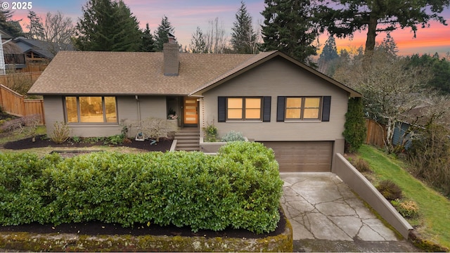 view of front of property featuring a shingled roof, fence, a chimney, driveway, and an attached garage