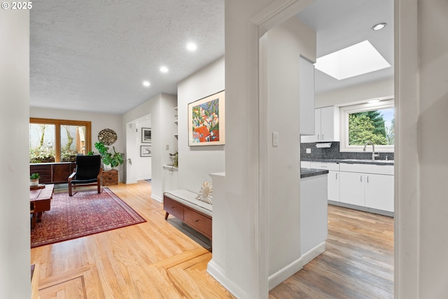 hall with a sink, plenty of natural light, a textured ceiling, and a skylight