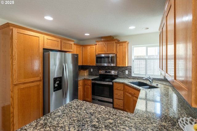 kitchen featuring brown cabinetry, tasteful backsplash, a sink, dark stone countertops, and stainless steel appliances