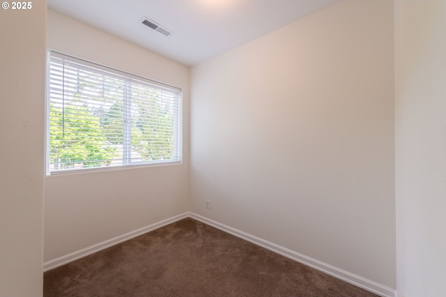 spare room featuring baseboards, dark carpet, and visible vents