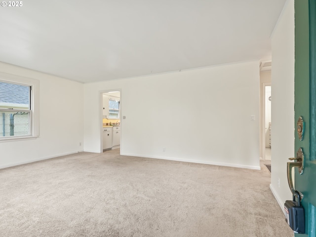 spare room featuring plenty of natural light, light colored carpet, and baseboards