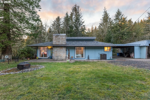 back house at dusk featuring central AC, a carport, a fire pit, and a lawn