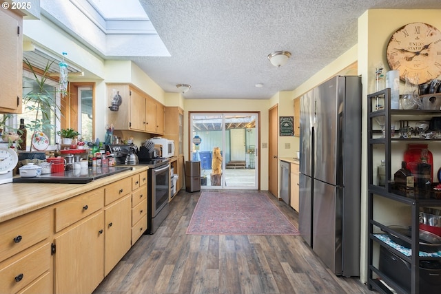 kitchen featuring dark wood-type flooring, light brown cabinetry, a skylight, a textured ceiling, and appliances with stainless steel finishes