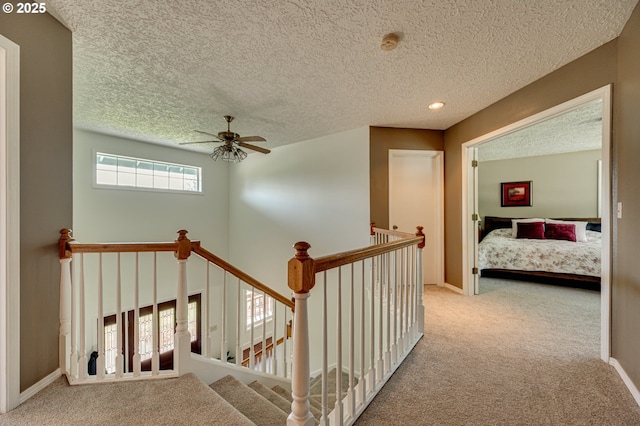 hallway featuring carpet flooring, a textured ceiling, an upstairs landing, baseboards, and recessed lighting
