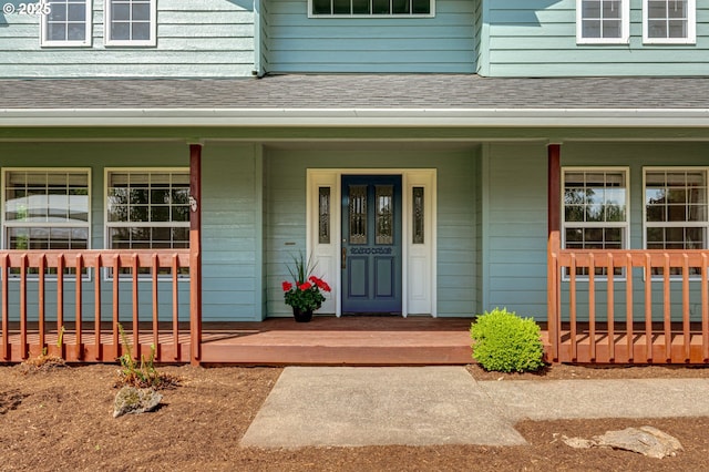 doorway to property featuring covered porch and a shingled roof